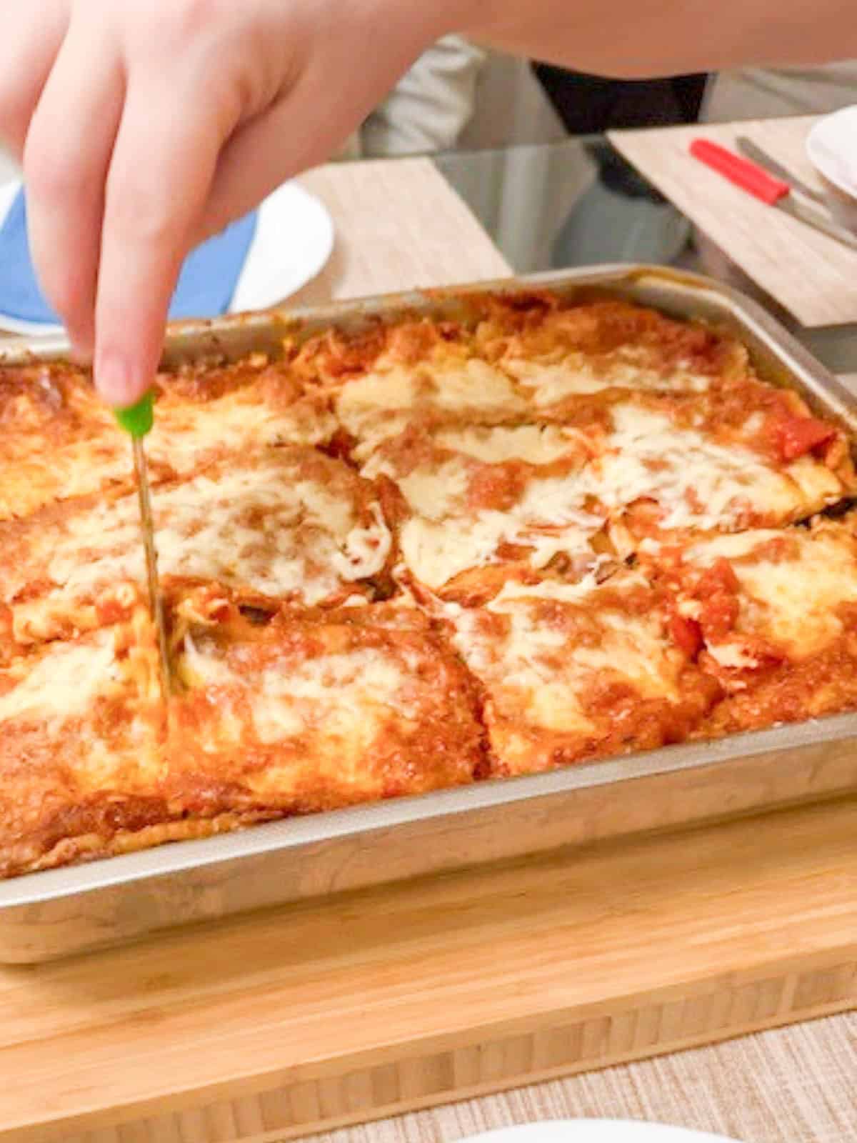 Cutting eggplant parmesan on the tray.