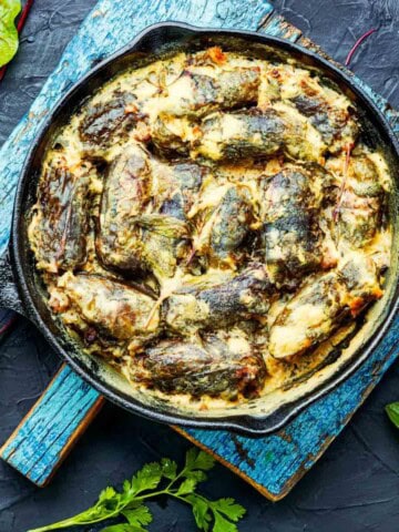 Stuffed grape leaves with lemon dill sauce in a black cast iron on top of a blue wood board.