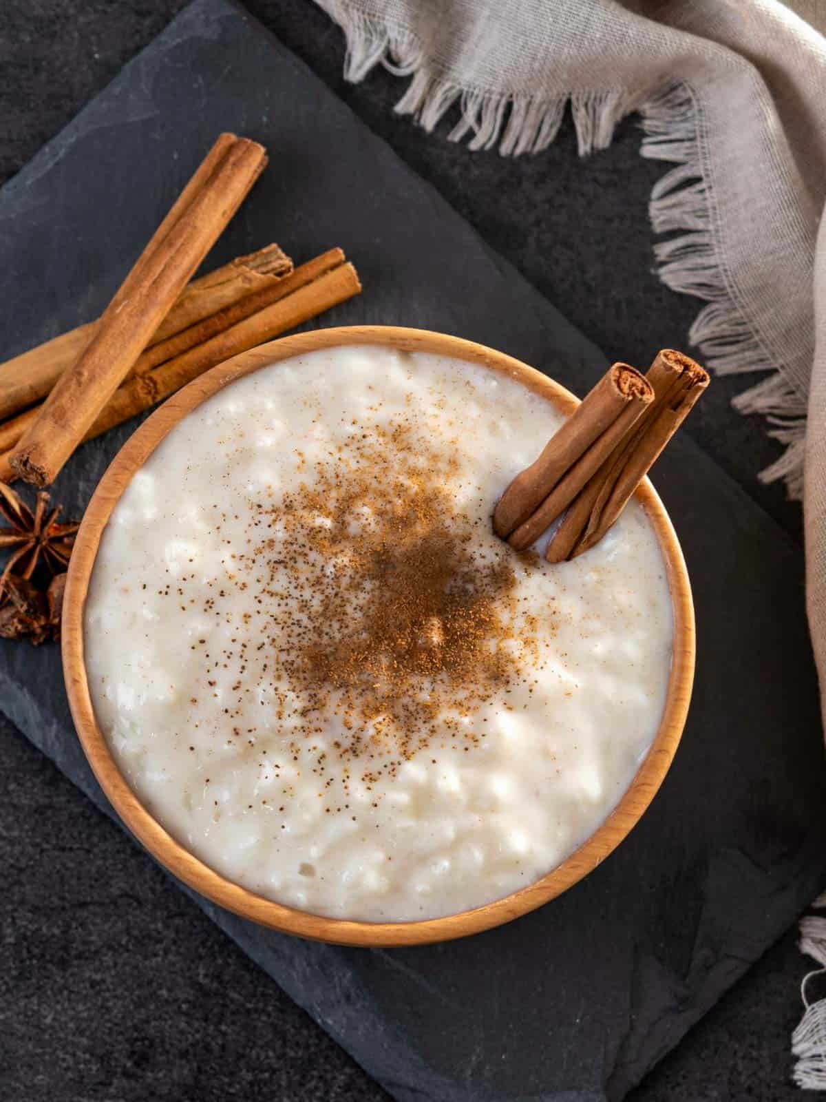 Rice pudding in a wooden bowl with anise, cinnamon stick and cinnamon powder on top