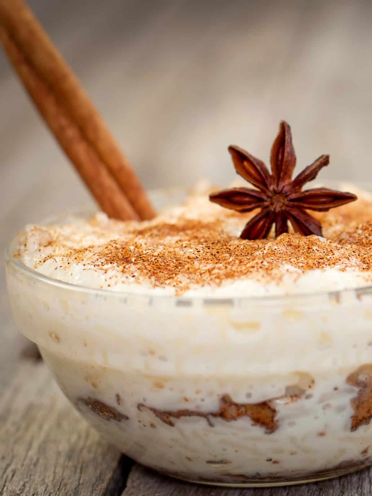 Rice pudding in a clear bowl with anise, cinnamon stick and cinnamon powder on top