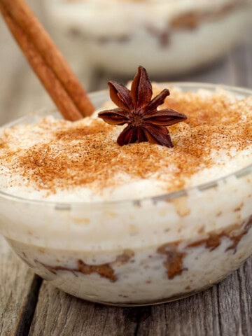 Rice pudding in a clear bowl with anise, cinnamon stick and cinnamon powder on top